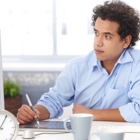 Young designer in blue shirt, using digital tablet at office, looking at screen, working.