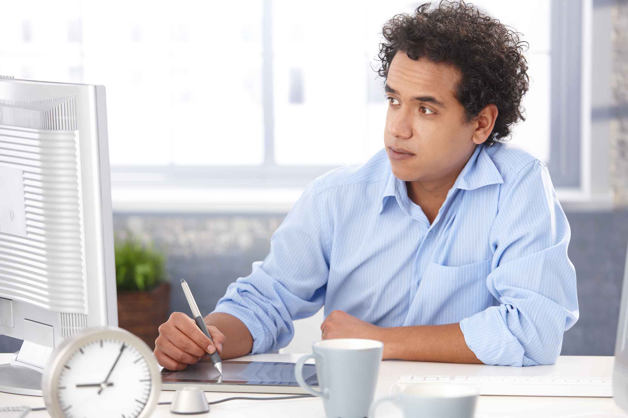 Young designer in blue shirt, using digital tablet at office, looking at screen, working.