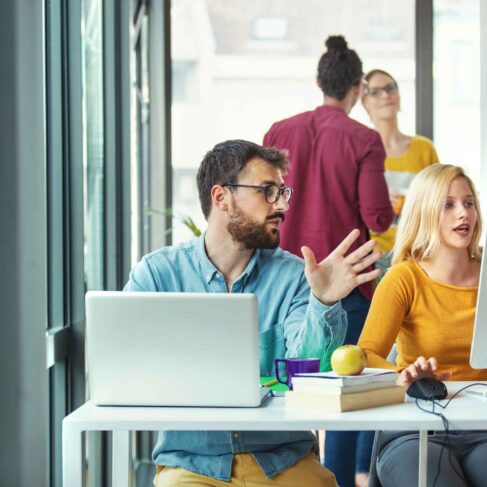 Closeup front view of group of young software engineer working at a small startup office. Two people in the foreground are in focus. More experienced employee is providing some guidance to his colleague.