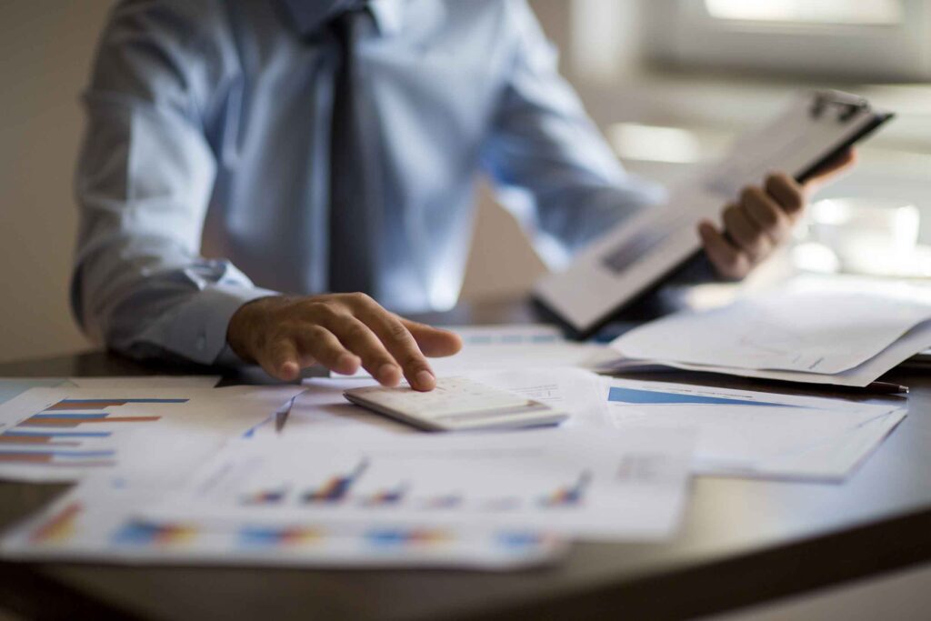 Business man using calculator with computer laptop, budget and loan paper in office.