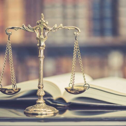 Judge gavel or a hammer and a base used by a judge person on a desk in a courtroom with blurred weight scale of justice, bookshelf background behind.