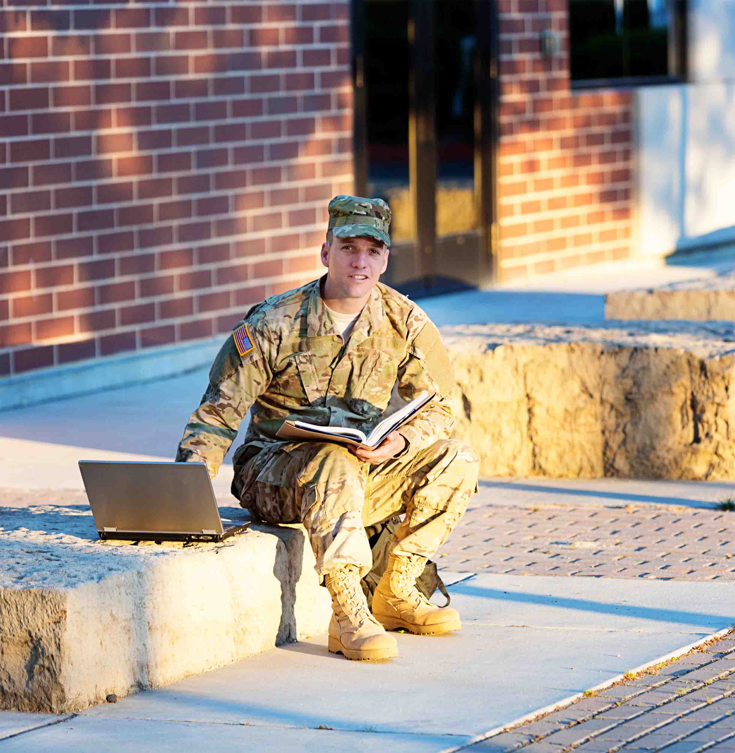 US soldier with laptop in front of campus.