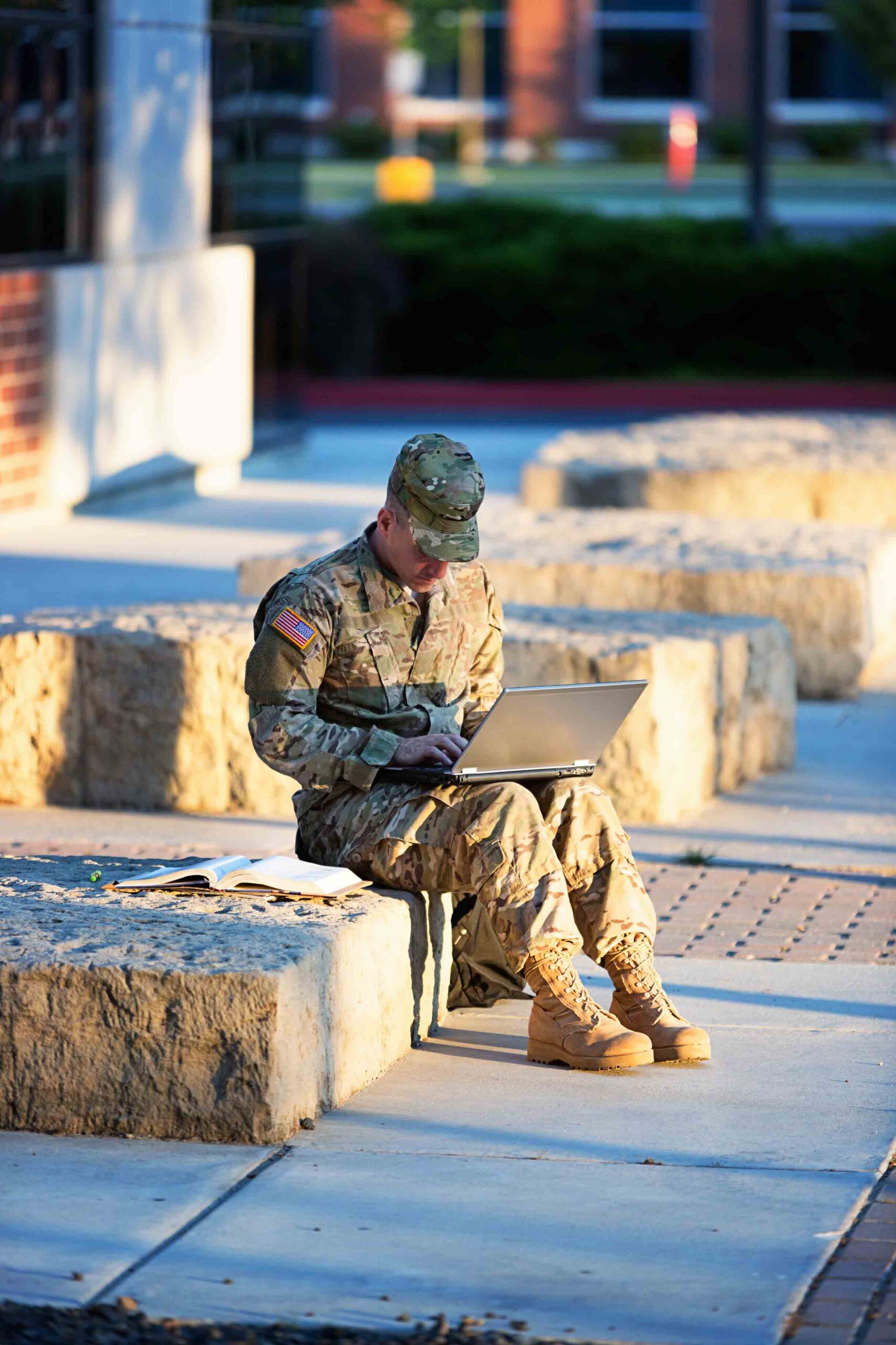 US soldier studying on laptop in front of campus.