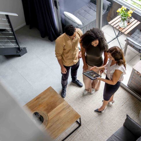 High angle view of a couple discussing details of a house with their real estate agent while looking at a brochure using a digital tablet