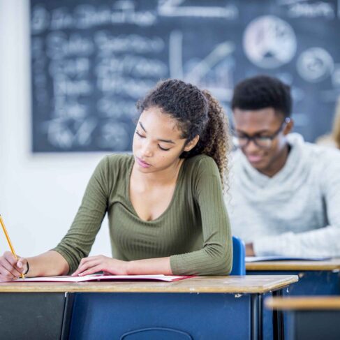 A group of high school students are indoors in their classroom. They are writing tests while sitting at their desks.