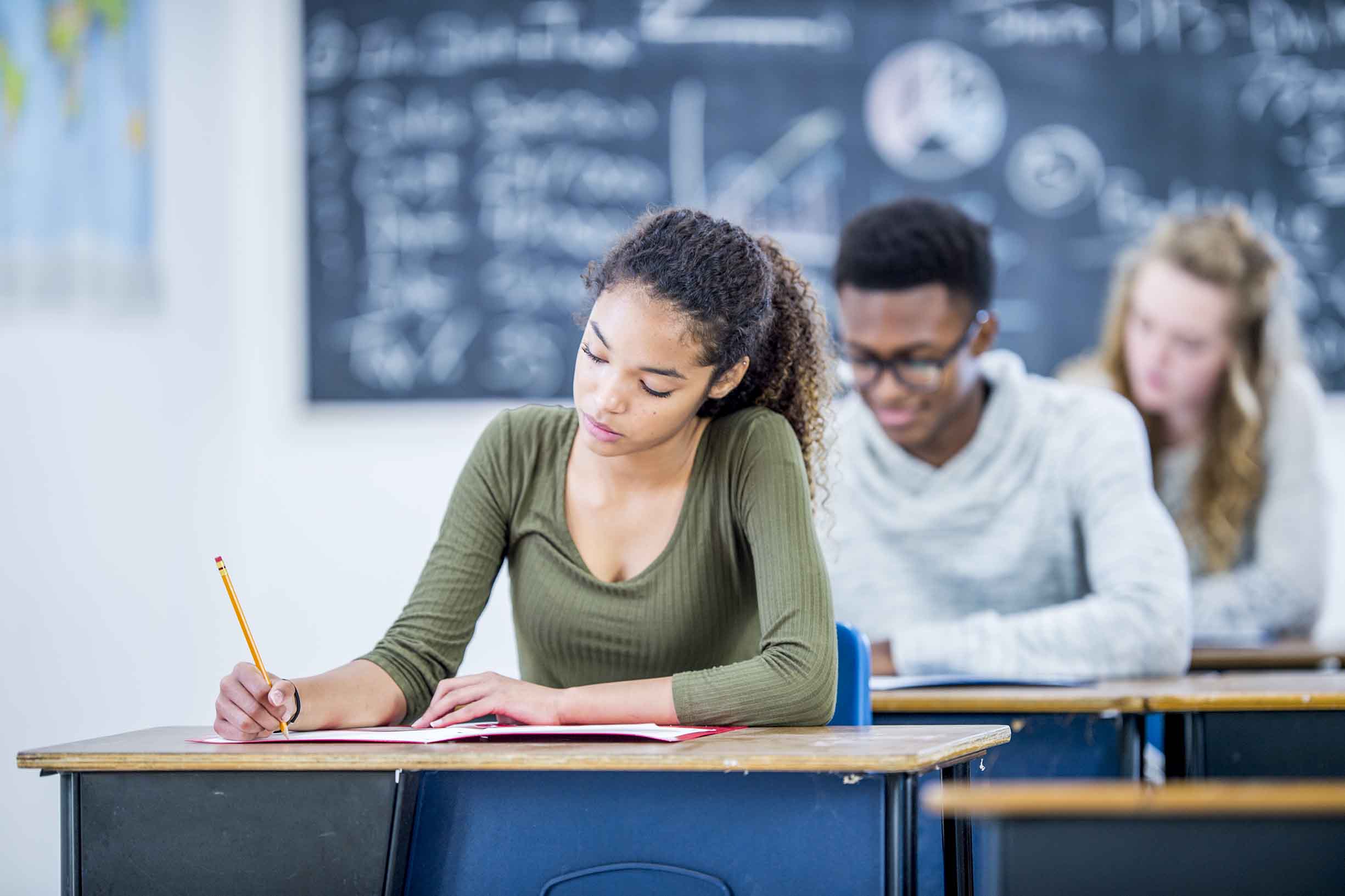 A group of high school students are indoors in their classroom. They are writing tests while sitting at their desks.