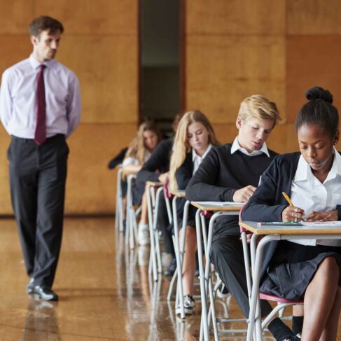 Teenage Students Sitting Examination With Teacher Invigilating