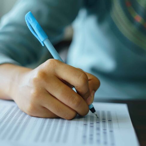 Close up of high school student holding a pen writing on answer sheet paper in the examination room.