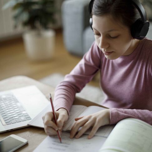 Smiling teenage girl with wireless headphones using laptop for studying at home
