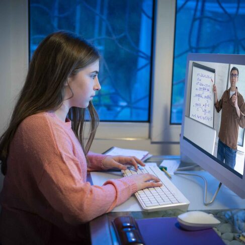 Teen student E-learning with teacher teleconference video call on computer at evening in her home living room table