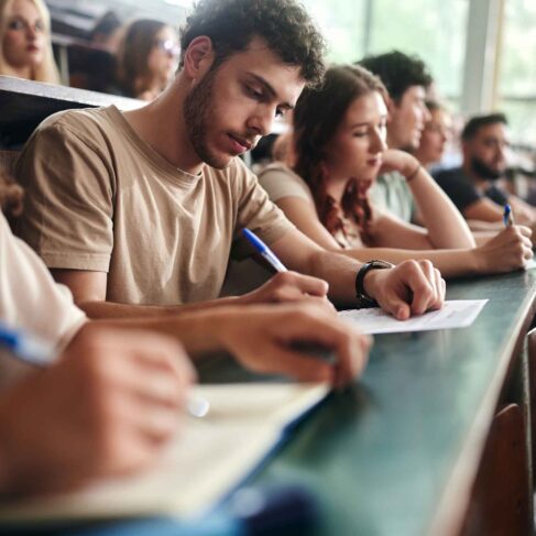 Male student and his classmates writing an exam during a class in amphitheater.