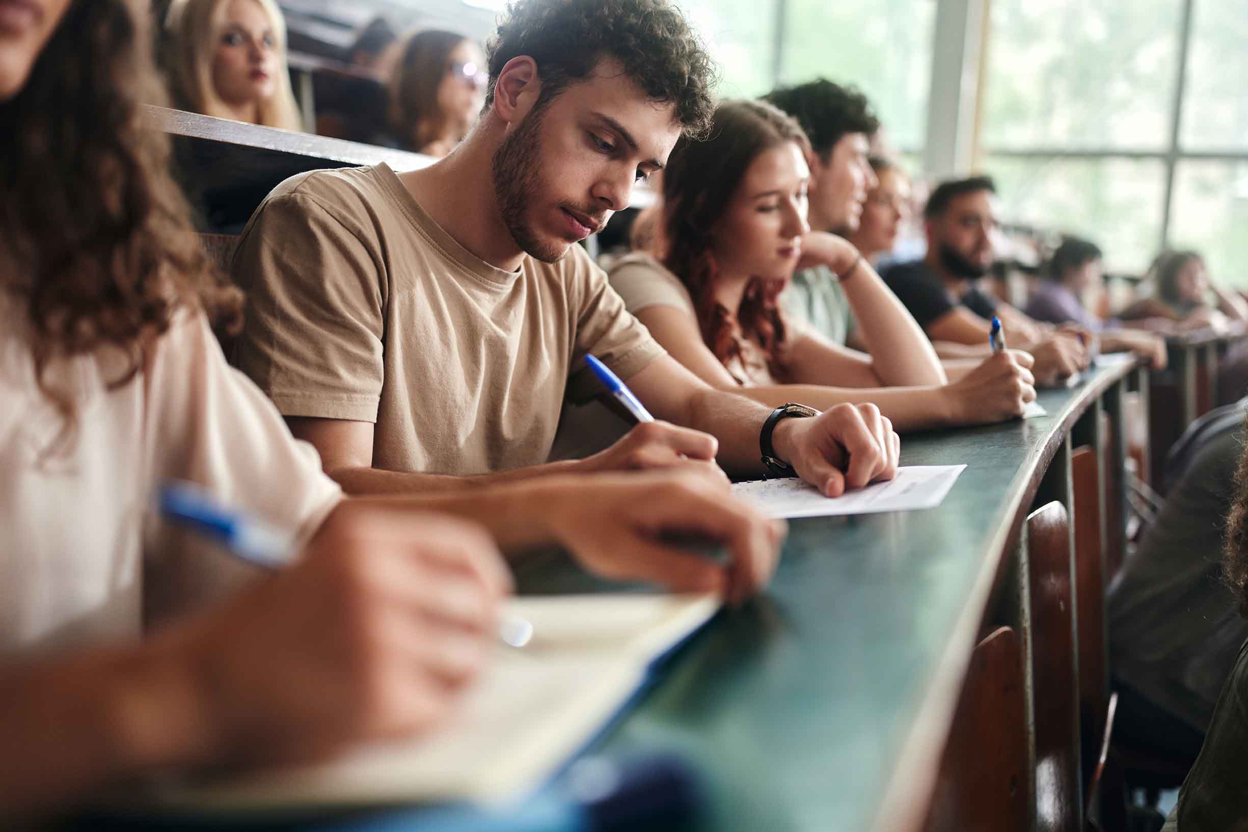 Male student and his classmates writing an exam during a class in amphitheater.