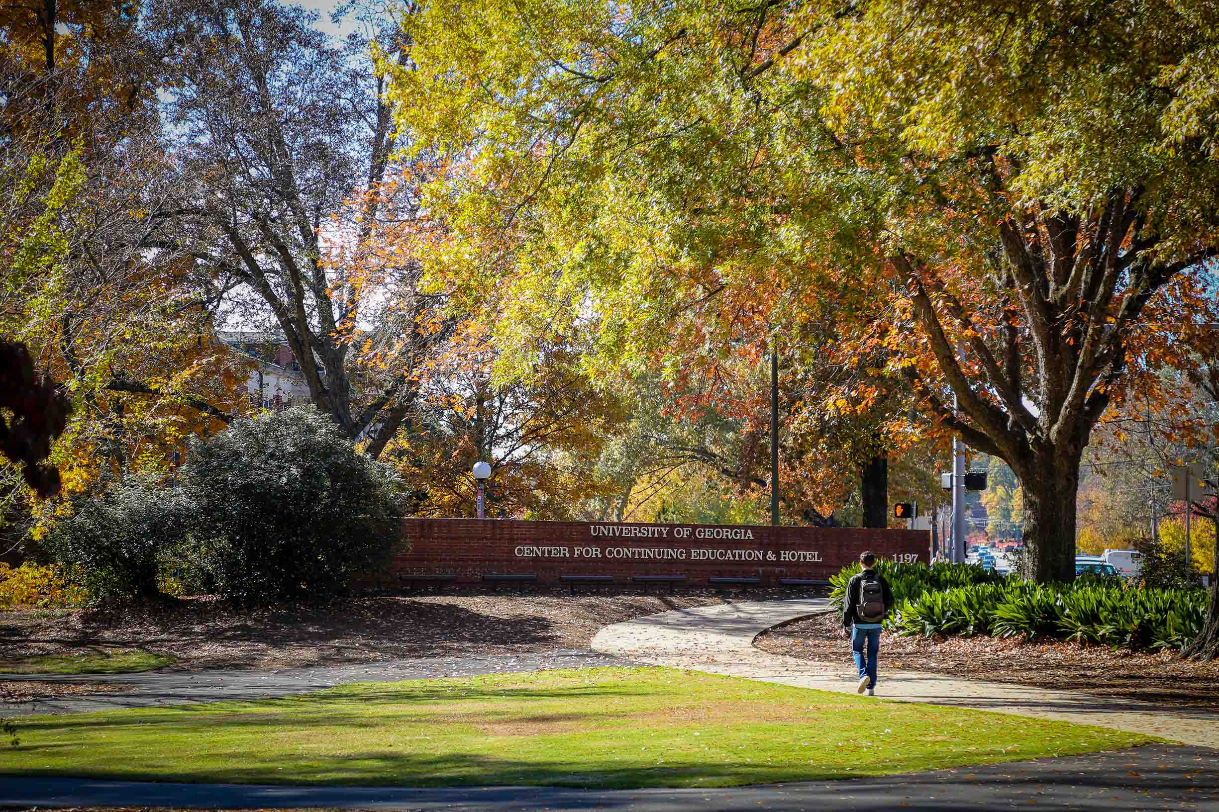 View of the University of Georgia sign made of brick that states Center for Continuing Education & Hotel with a student walking towards the building sign