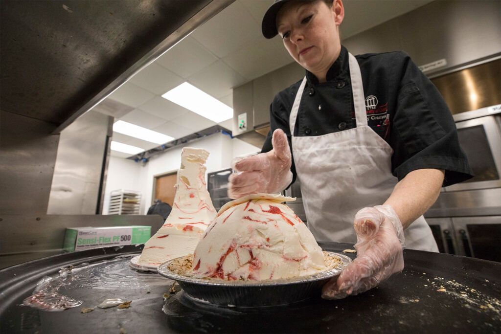 Kelly Cramer, a baker with the Georgia Center for Continuing Education & Hotel, adds ice cream to a meringue coconut crust to make strawberry ice cream pie in the kitchen