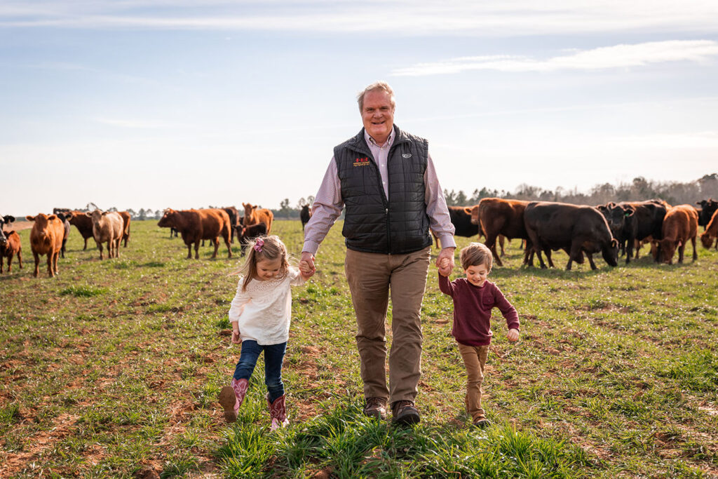 Keith Kelly walks with his grandchildren on the Rock House Creamery family farm in a pasture with brown cows.