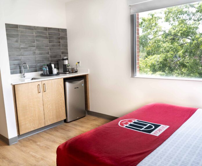 View of lower cabinets with fridge, sink and coffee pot beside a window with a tree outside.
