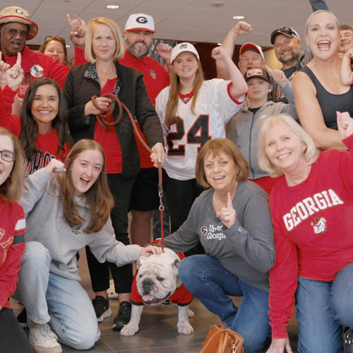 Georgia fans posing and cheering beside UGA bulldog mascot.
