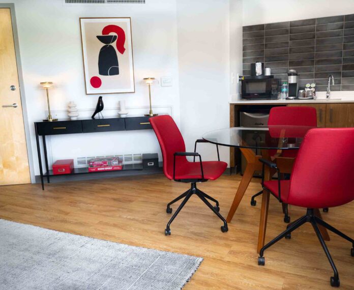 view of the Vice President's Queen suite with three red chairs and glass table and cabinets in the background with a fridge, sink, microwave, and coffee maker on the counter.