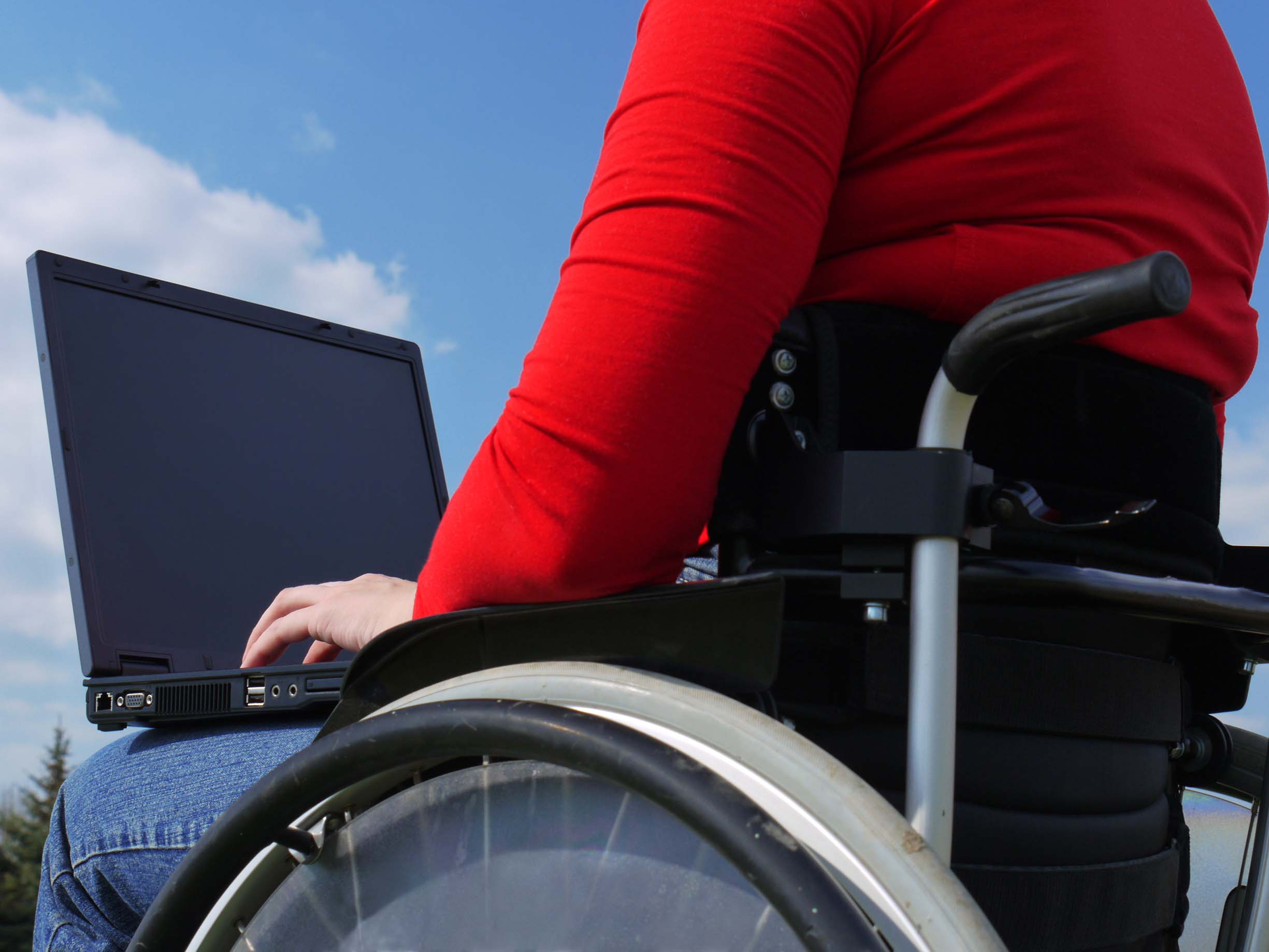 Handicapped woman on wheelchair using laptop outdoors
