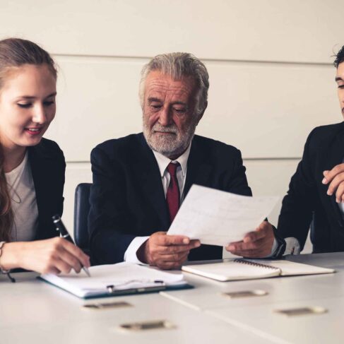 Senior old executive manager working with young businesspeople in office meeting room. Old man is the company leader sitting with secretary and translator.