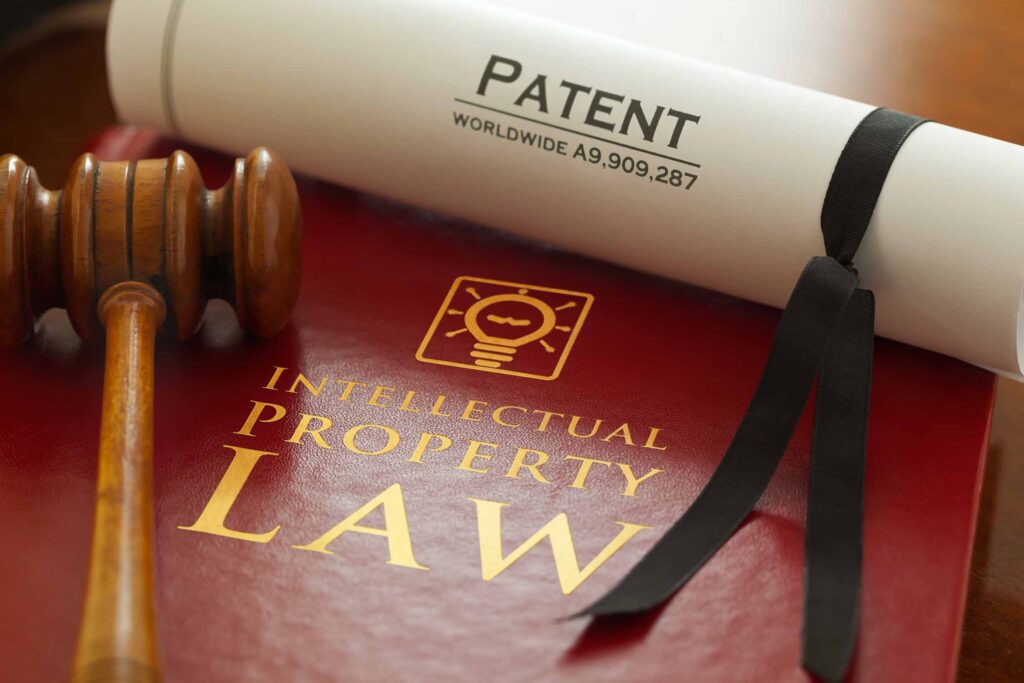 Red leather Intellectual Property Law book with with gold embossed type and iconic light bulb, ideas icon logo, with a judges gavel and a generic A4 Patent document. Note patent number is fictitious.