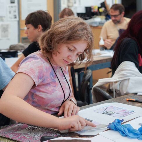 Student creating a print with other students in a classroom