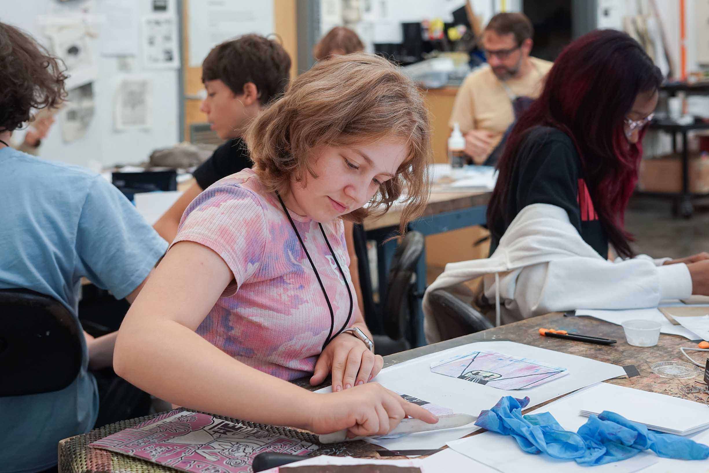 Student creating a print with other students in a classroom