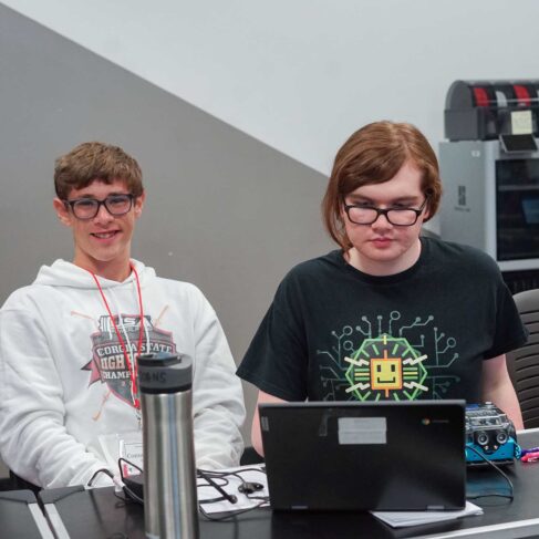 Two students working on programing their robots in a classroom.