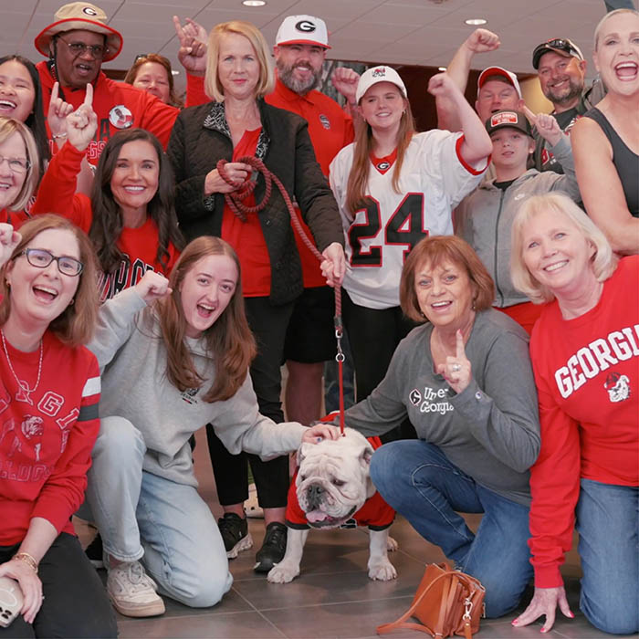 Georgia fans posing and cheering beside UGA bulldog mascot.
