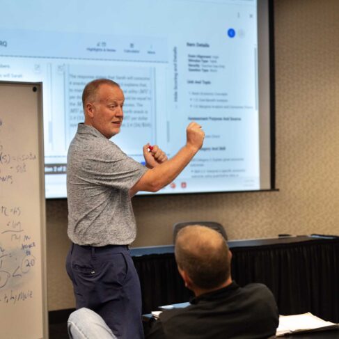 Instructor standing in front a screen with a PowerPoint presentation displayed and beside a erase board.