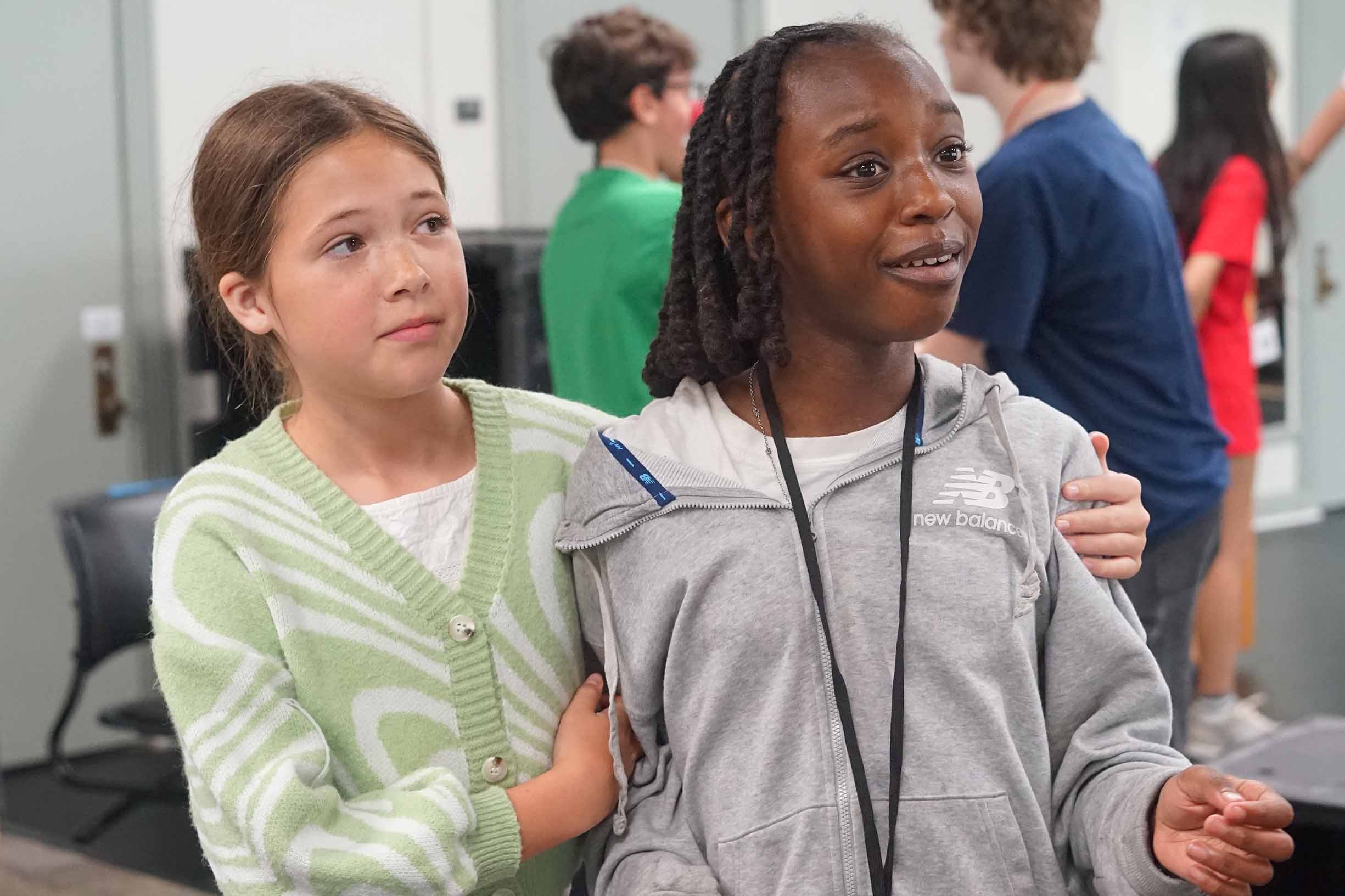 two students acting in a classroom wearing a green and white sweater and gray sweatshirt.