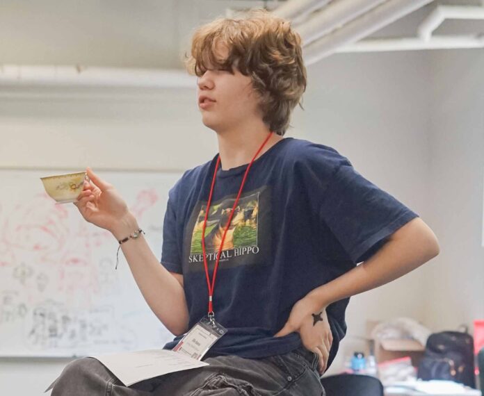 A young student acting out a scene in a classroom while holding a tea cup