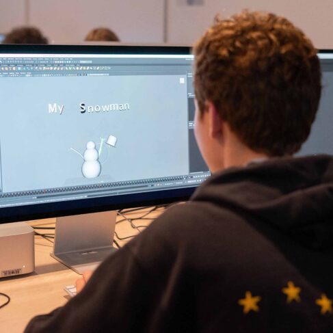 Student looking at the computer screen with a drawing of a snowman in a classroom