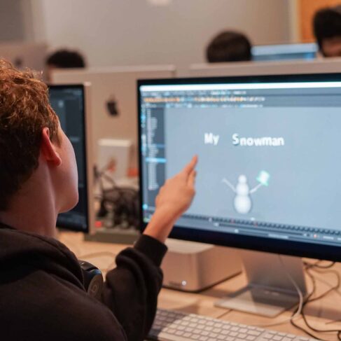 Student pointing at the computer screen with a drawing of a snowman in a classroom