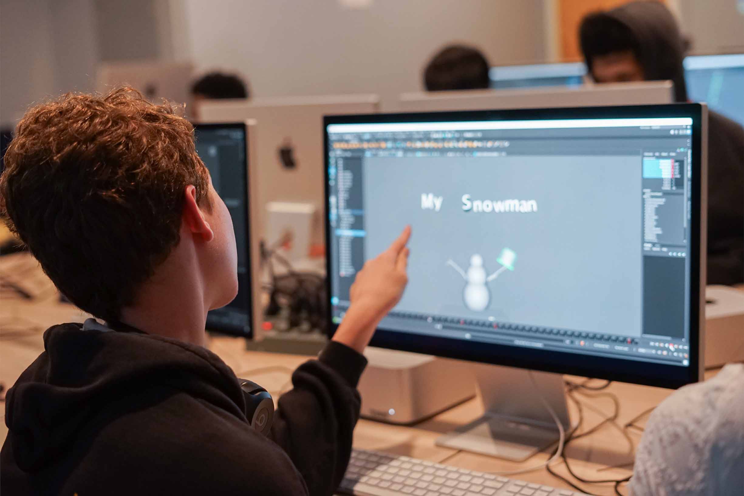 Student pointing at the computer screen with a drawing of a snowman in a classroom