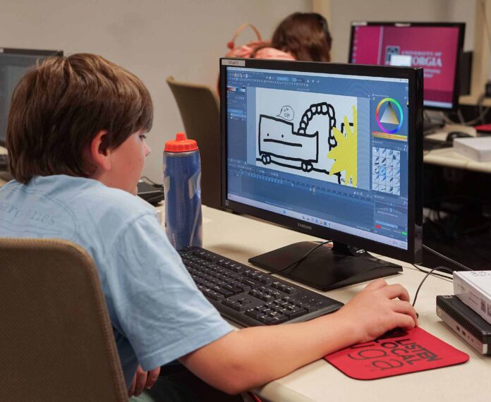 A student using his computer mouse to draw an image on his computer screen sitting in a computer lab.
