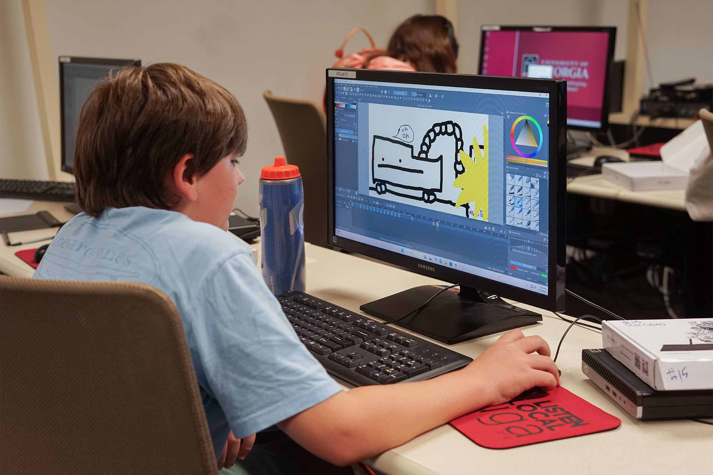 A student using his computer mouse to draw an image on his computer screen sitting in a computer lab.