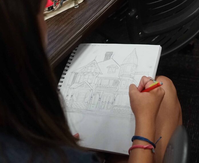 Student drawing a building in a notebook.