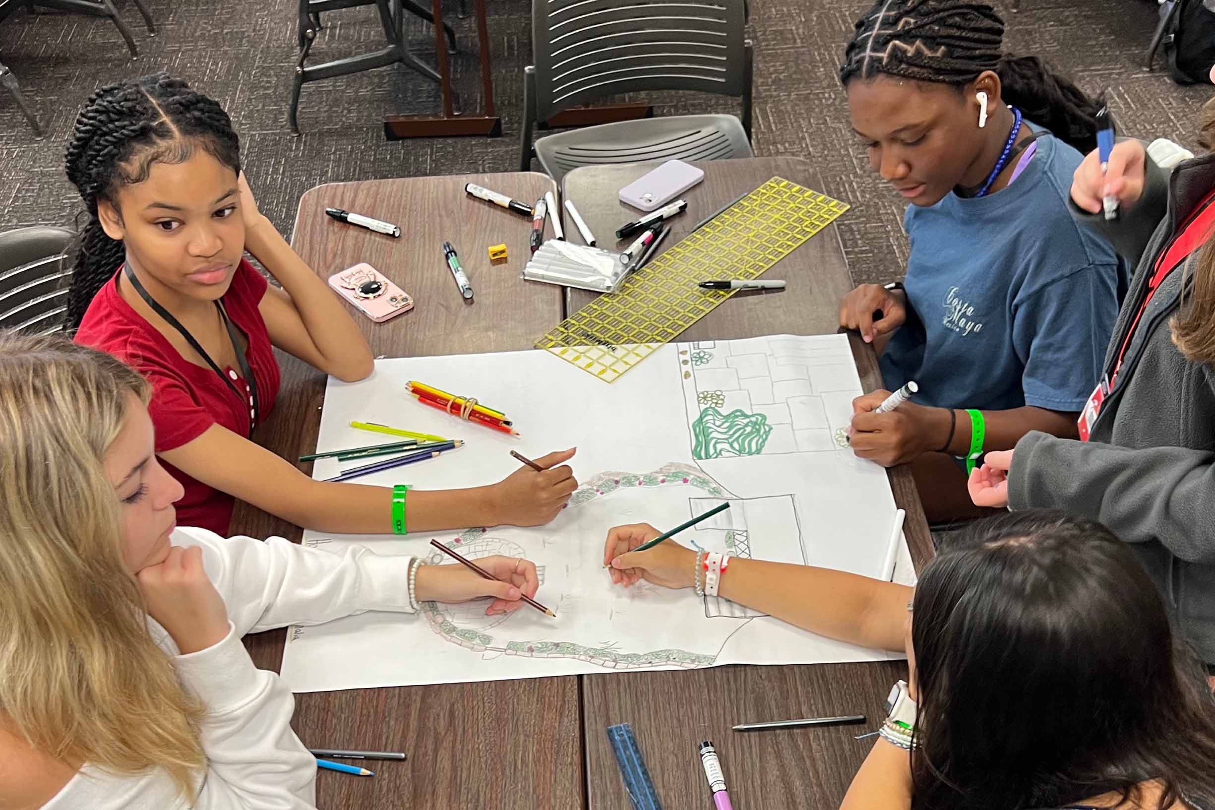 five students designing a building structure on a piece of paper on a table in a classroom