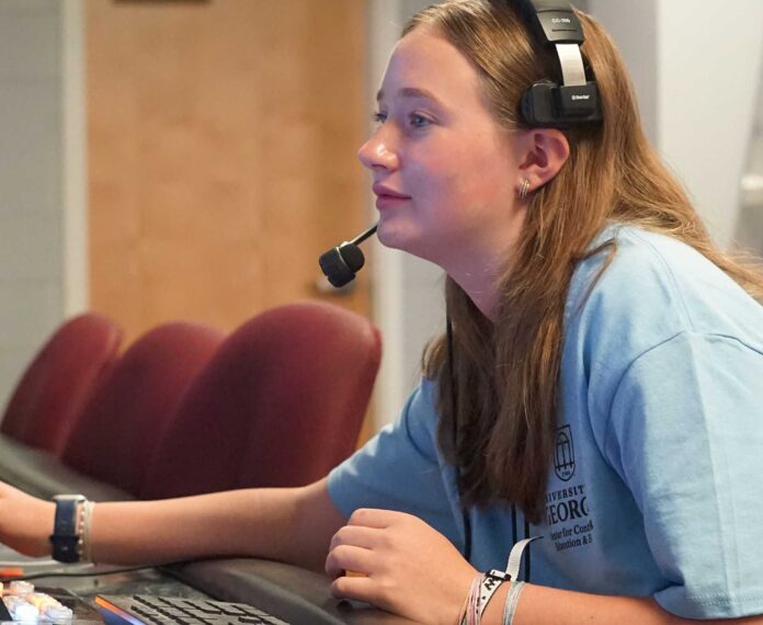 A student sitting at a control panel wearing headphones in a studio.