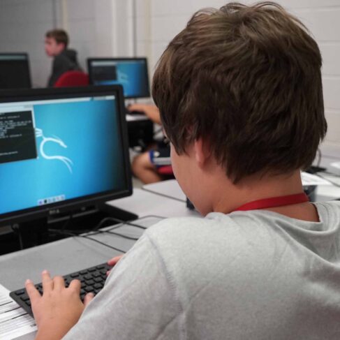 Male student sitting at a desk with a computer screen displaying code.