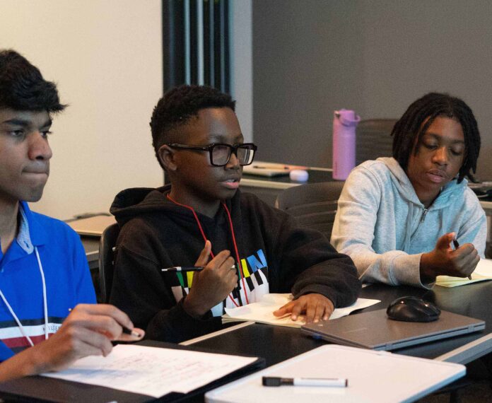 Three students sitting at a table discussing cybersecurity in a classroom
