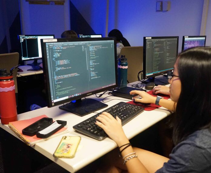 Female student looking at code on a computer screen sitting in a dark classroom