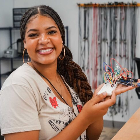 Student holding a electrical board with wires in a classroom