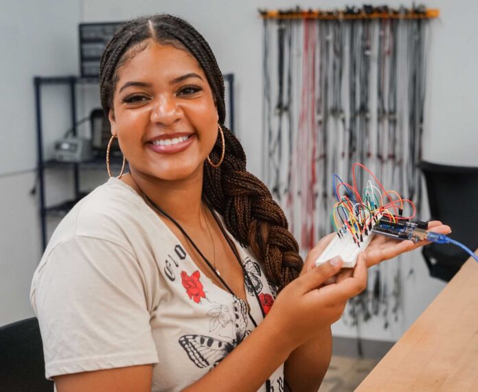 Student holding a electrical board with wires in a classroom