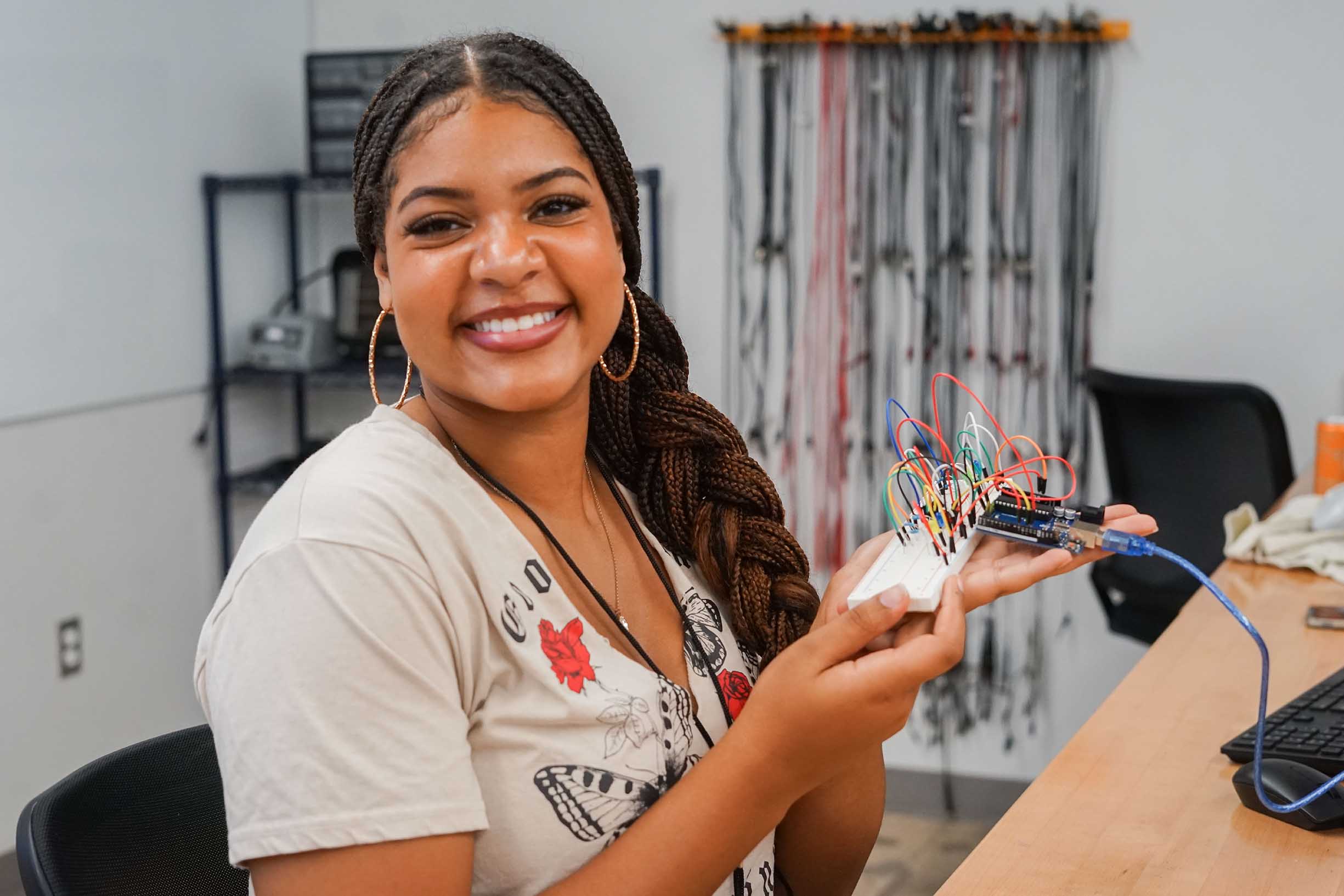 Student holding a electrical board with wires in a classroom