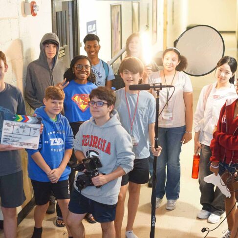 A group of students on a production set holding various objects needed for filming.