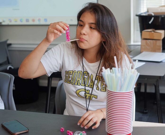 Student stacking dice on a Popsicle stick in her mouth in a classroom