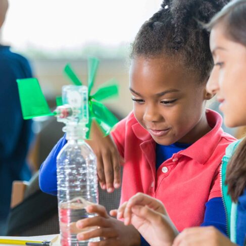 Students are building a windmill from a water bottle during an after school science program in a classroom