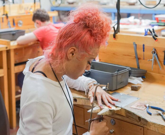 Student creating jewelry with a saw at a workbench